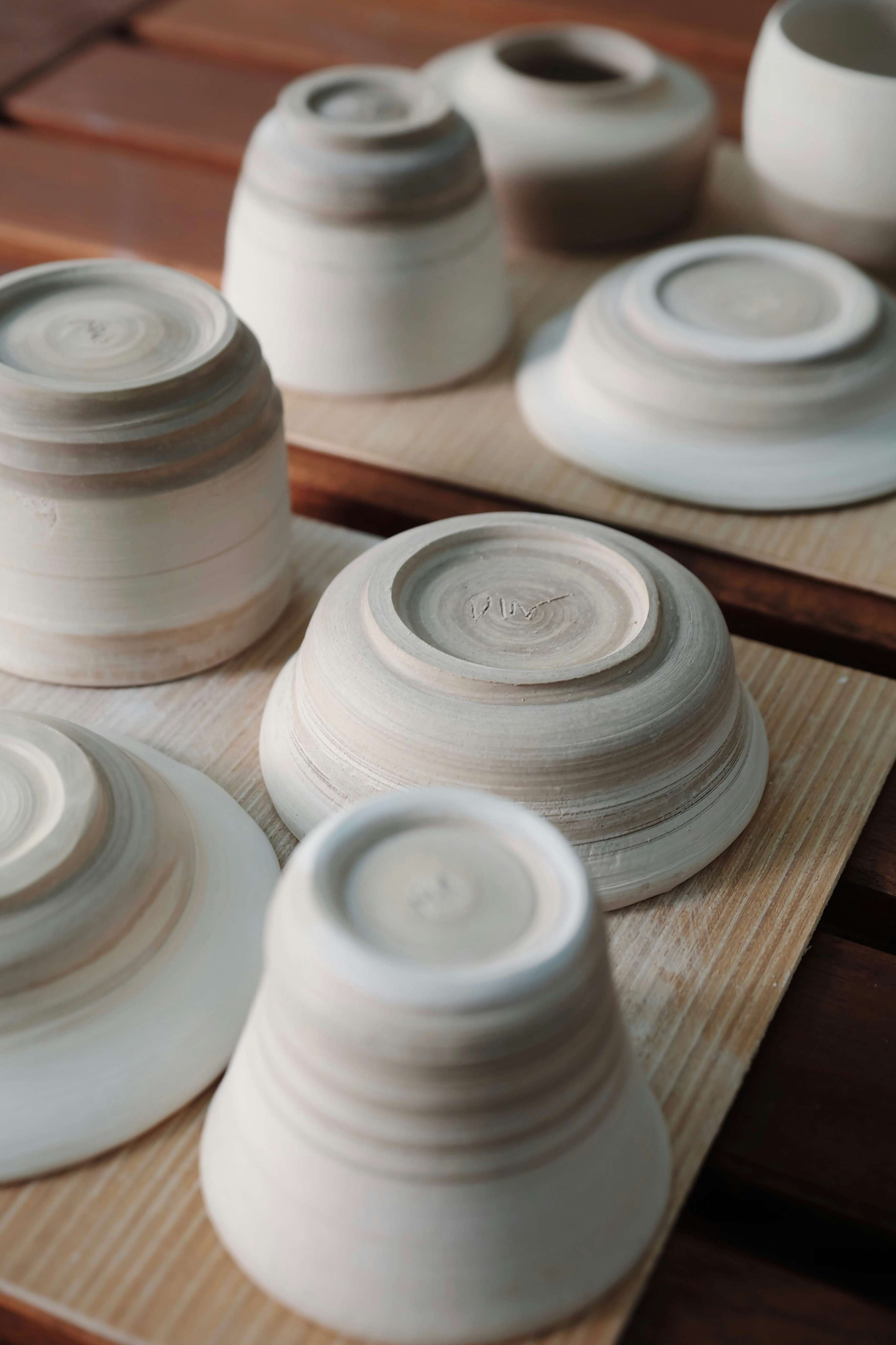 Rows of upturned unglazed ceramic bowls drying upside down on wooden boards after throwing.