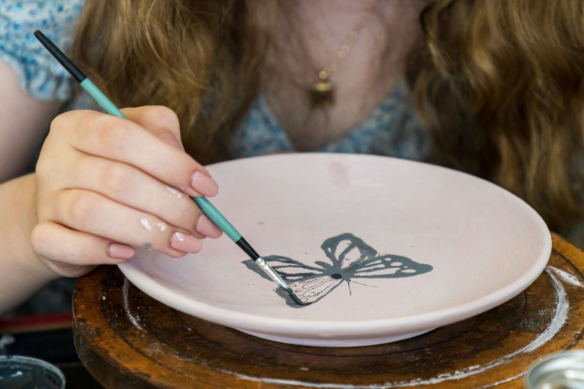 A young student using a paintbrush to decorate a ceramic plate in a kids' pottery workshop.